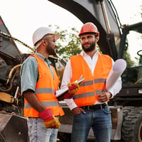 Two construction workers having a conversation in front of heavy equipment