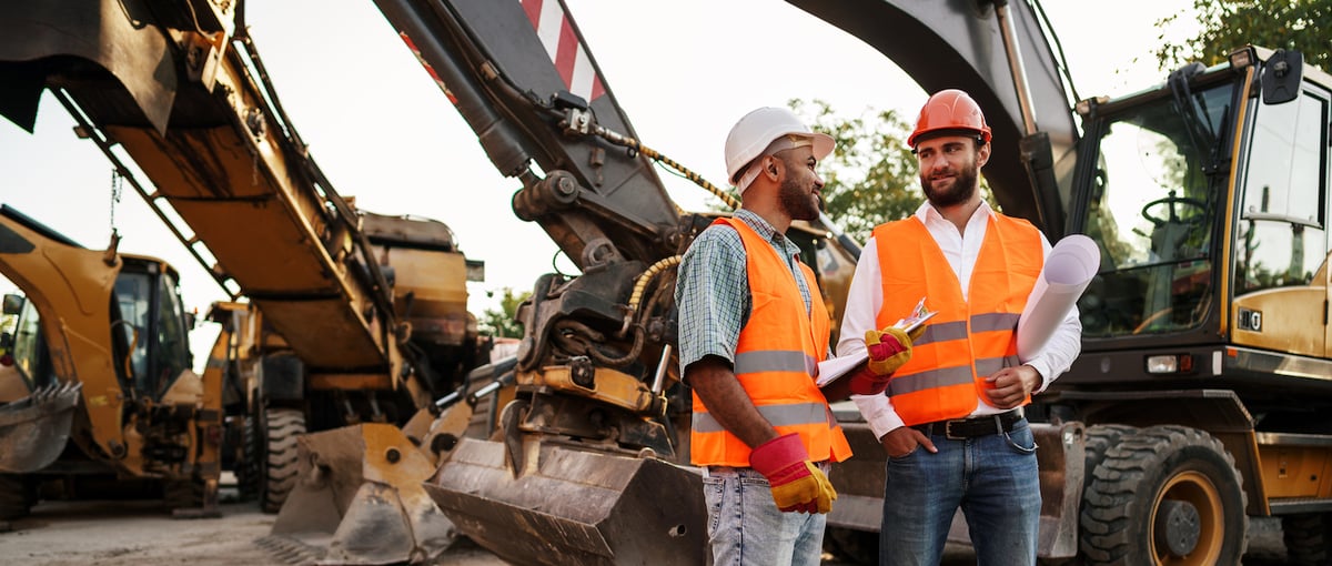two construction workers standing in front of construction equipment